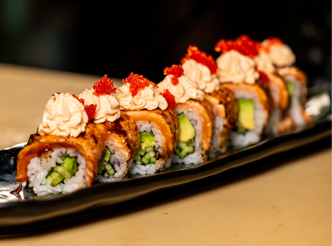 sushi rolls - Restaurant Pescăruș Sushi rolls lined on a black plate topped with creamy dollops and red tobiko, with cucumber and avocado inside.