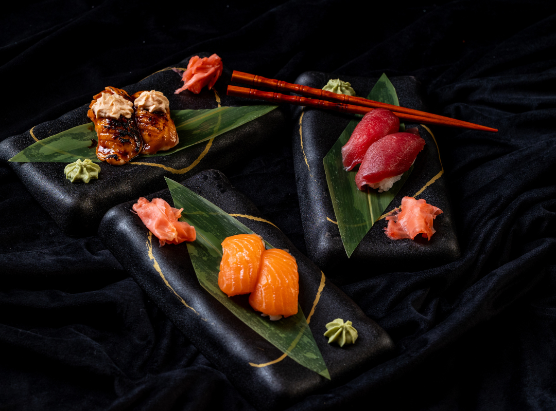 nigiri sushi - Restaurant Pescăruș Assorted nigiri sushi on black stones with green leaves and wasabi, arranged on a dark fabric backdrop.
