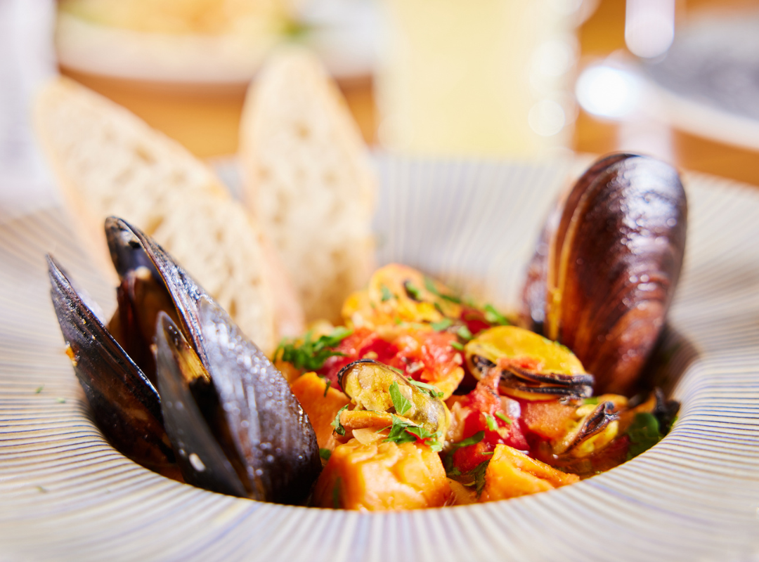 scoici - Restaurant Pescăruș Seafood stew with mussels, shrimp or fish chunks, herbs, and bread in a wide striped bowl.
