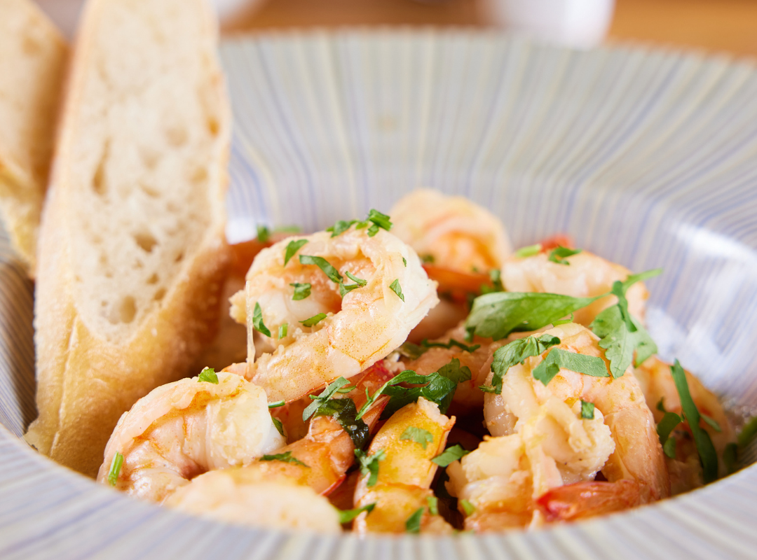 supa creveti - Restaurant Pescăruș Shrimp dish garnished with chopped parsley in a striped bowl, with slices of bread on the side.